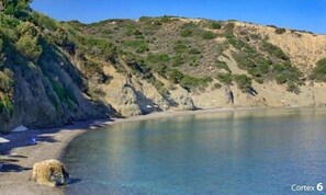 A coastal landscape with a beach, cliffs, and clear water.