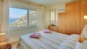 A bedroom with a bed, a dresser, a window with a view of a cliff, and an air conditioning unit.