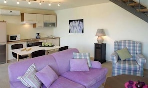 A living room with a purple sofa, a plaid armchair, a dining table with chairs, a kitchen area, and a staircase. - One Bedroom Villa With Private Seawater Pool! Just 150 Meters From the sea (Agios Nikolaos)