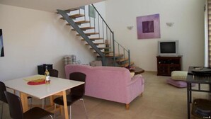 A living room with a staircase, a pink sofa, a TV, and a dining area. - One Bedroom Villa With Private Seawater Pool! Just 150 Meters From the sea (Agios Nikolaos)