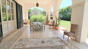 Een terras buiten met een ronde tafel en stoelen, een bank en potplanten.