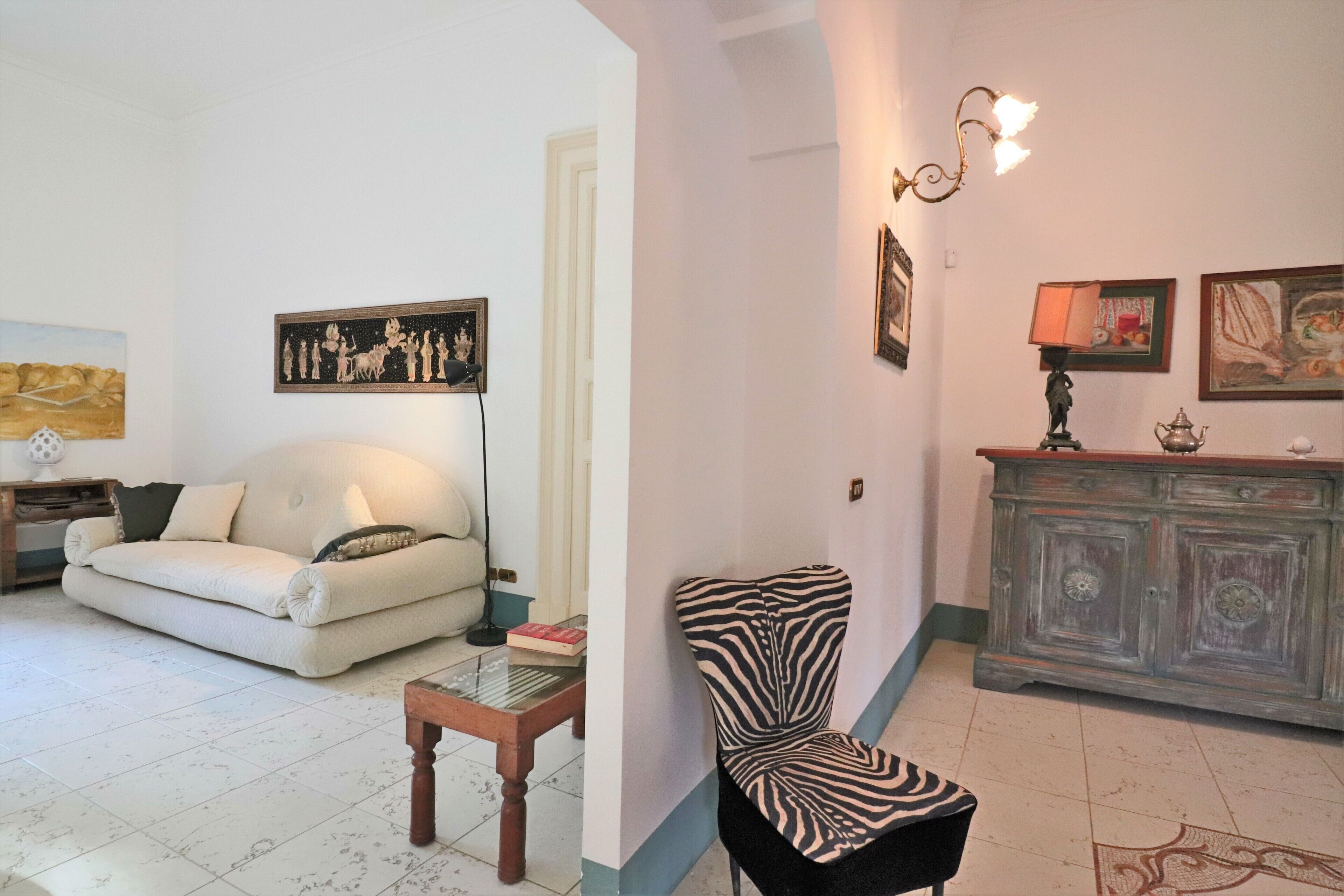 A living room with a sofa, a zebra-patterned chair, a wooden coffee table, a cabinet, and wall art.