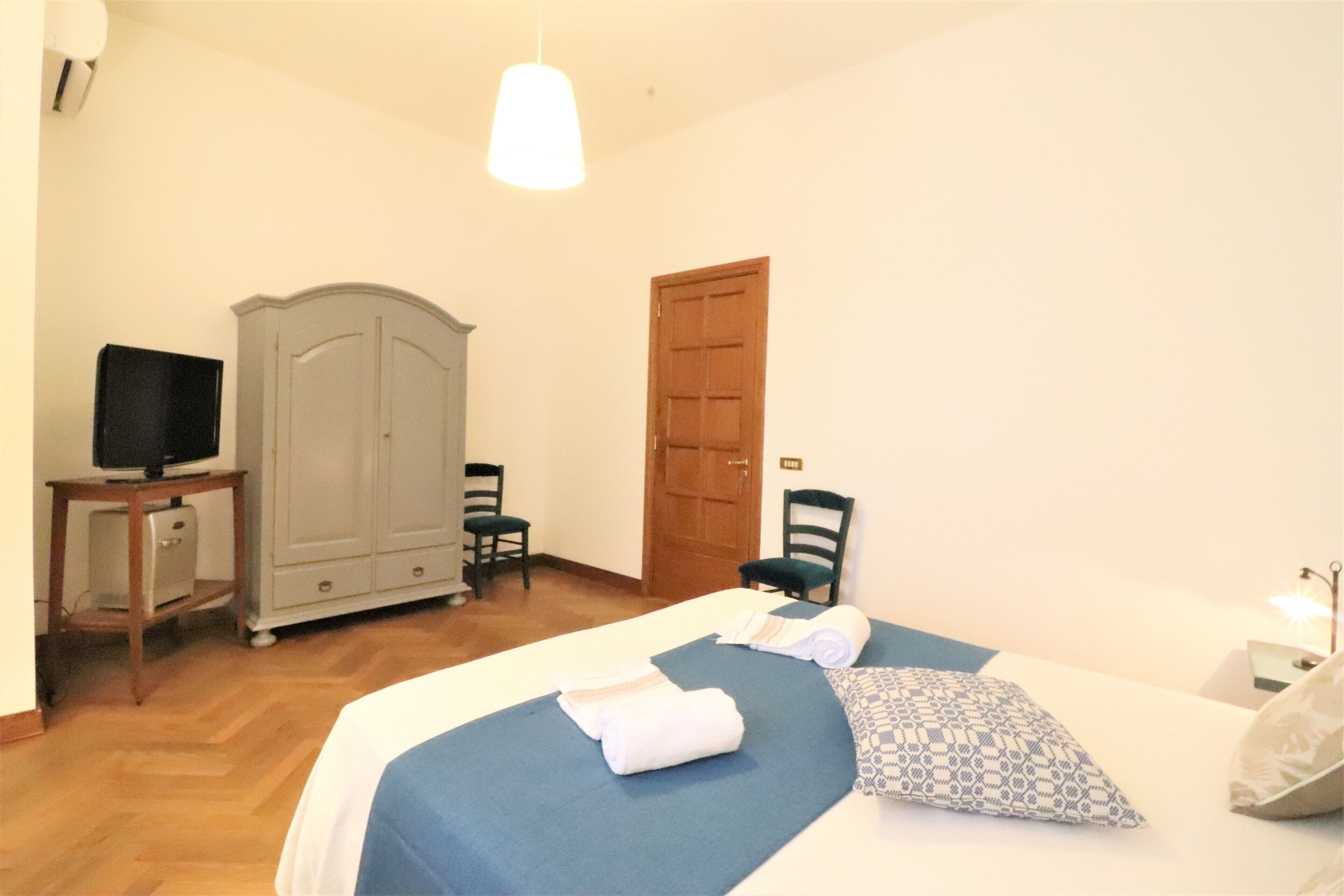 Une chambre d’hôtel avec un lit, une armoire, un téléviseur posé sur une petite table et une porte.