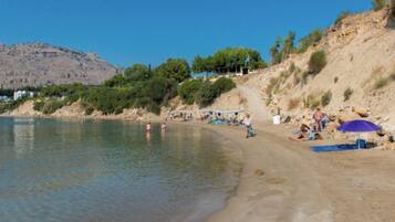 A beach with people sunbathing and swimming, a sandy shore, and a mountain in the background.