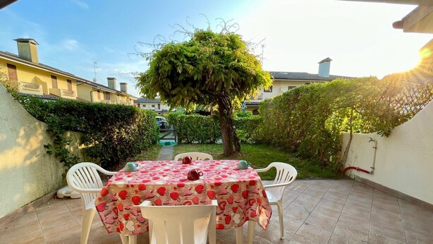 Eine Terrasse mit Tisch und Stühlen, umgeben von Grünpflanzen und Blick auf angrenzende Gebäude.
