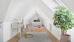 A modern loft bedroom with a sloped ceiling, a white desk with a chair, a bedside table, a bed with a quilted cover, and a large potted plant. - Regent 9 - Great Apt With Terrace in City Centre (Copenhagen)
