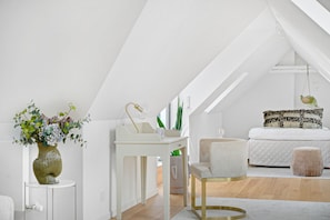 A modern bedroom with a sloped ceiling, a white bed, a bedside table, a chair, a small stool, and a vase with flowers. - Regent 9 - Great Apt With Terrace in City Centre (Copenhagen)