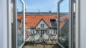 A balcony with a table and chairs, a view of a building with a red-tiled roof, and a clear sky. - Regent 9 - Great Apt With Terrace in City Centre (Copenhagen)