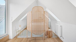 A modern loft bedroom with a sloped ceiling, a rattan chair, a small table, and a radiator. - Regent 9 - Great Apt With Terrace in City Centre (Copenhagen)