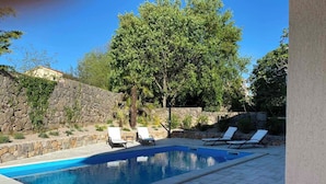 En swimmingpool med hvide liggestole og en stenvæg.