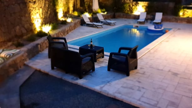 En swimmingpool med liggestole og et bord, omgivet af stenvægge og planter.