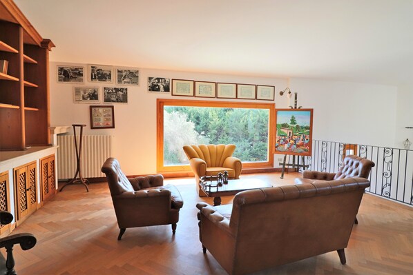 A spacious living room with a large window, leather sofas, a coffee table, and a bookshelf.