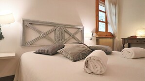 Une chambre à coucher avec un lit, des oreillers, une tête de lit, une fenêtre et une table de chevet avec une lampe.