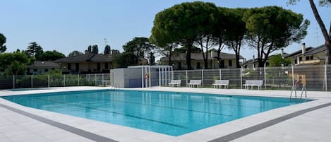 A rectangular swimming pool with a tiled deck, surrounded by a white fence and benches.