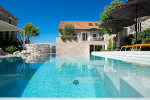 A clear swimming pool with a stone wall and a building with a red-tiled roof in the background. - Villa Lastva is a Five Star Seafront Luxury Villa With Privite Pool (Tivat)