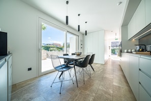 A modern kitchen with a dining area, featuring a large window, a bowl on the table, and a view of the outdoors. - Villa Lastva is a Five Star Seafront Luxury Villa With Privite Pool (Tivat)