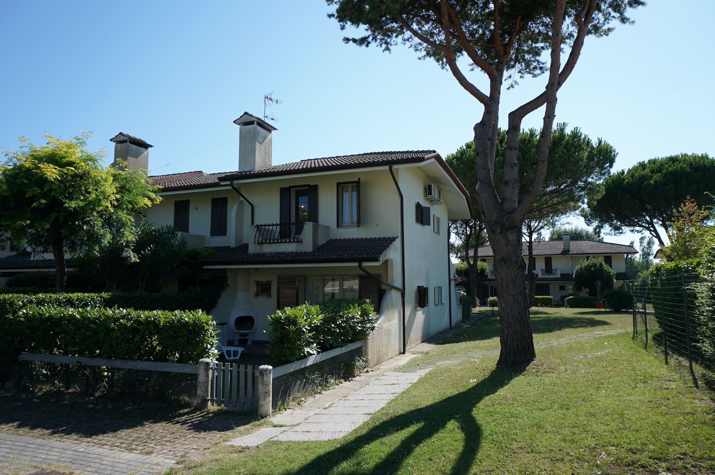 A two-story house with a balcony, surrounded by a well-maintained lawn and trees.
