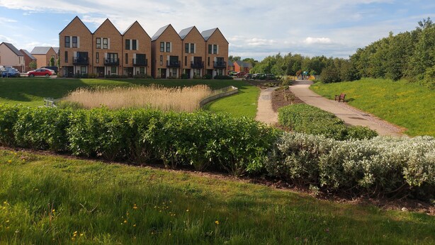 Una hilera de casas modernas de ladrillo con balcones, un área verde con un sendero y un banco.