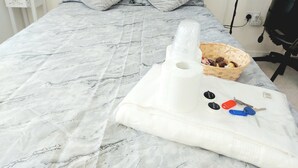 Una cama con una colcha estampada en mármol, dos almohadas, una cesta con objetos y un paquete con llaves y una etiqueta.