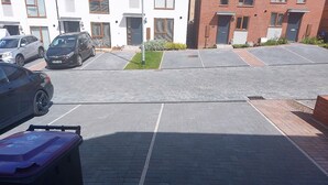 Un aparcamiento con varios coches, un edificio de ladrillo y una pequeña zona verde.