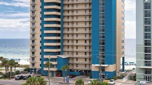 Ein mehrstöckiges Hotel mit blau-beiger Fassade, gelegen in Strandnähe mit Blick auf das Meer und Palmen.