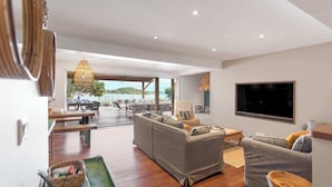 A spacious living area with a large sofa set, a dining table, and a TV mounted on the wall. - Villa Baltazar – Waterfront Luxury Villa Facing Pinel Islet, Saint Martin (Cul-de-Sac)