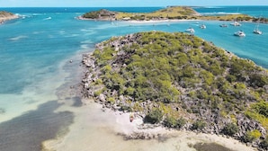 A tropical island with clear turquoise waters, rocky shores, and lush greenery. - Villa Baltazar – Waterfront Luxury Villa Facing Pinel Islet, Saint Martin (Cul-de-Sac)