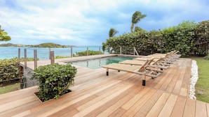 A wooden deck with lounge chairs, a pool, and a view of the sea. - Villa Baltazar – Waterfront Luxury Villa Facing Pinel Islet, Saint Martin (Cul-de-Sac)