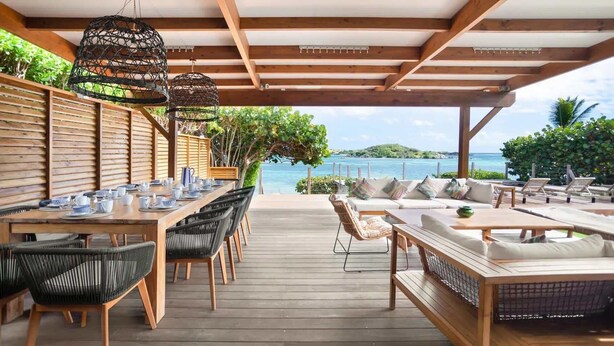 A wooden deck with a dining table set for tea, wicker chairs, and a sofa with cushions. - Villa Baltazar – Waterfront Luxury Villa Facing Pinel Islet, Saint Martin (Cul-de-Sac)
