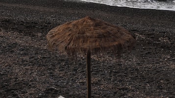 På stranden, svart sandstrand, solstolar och parasoller