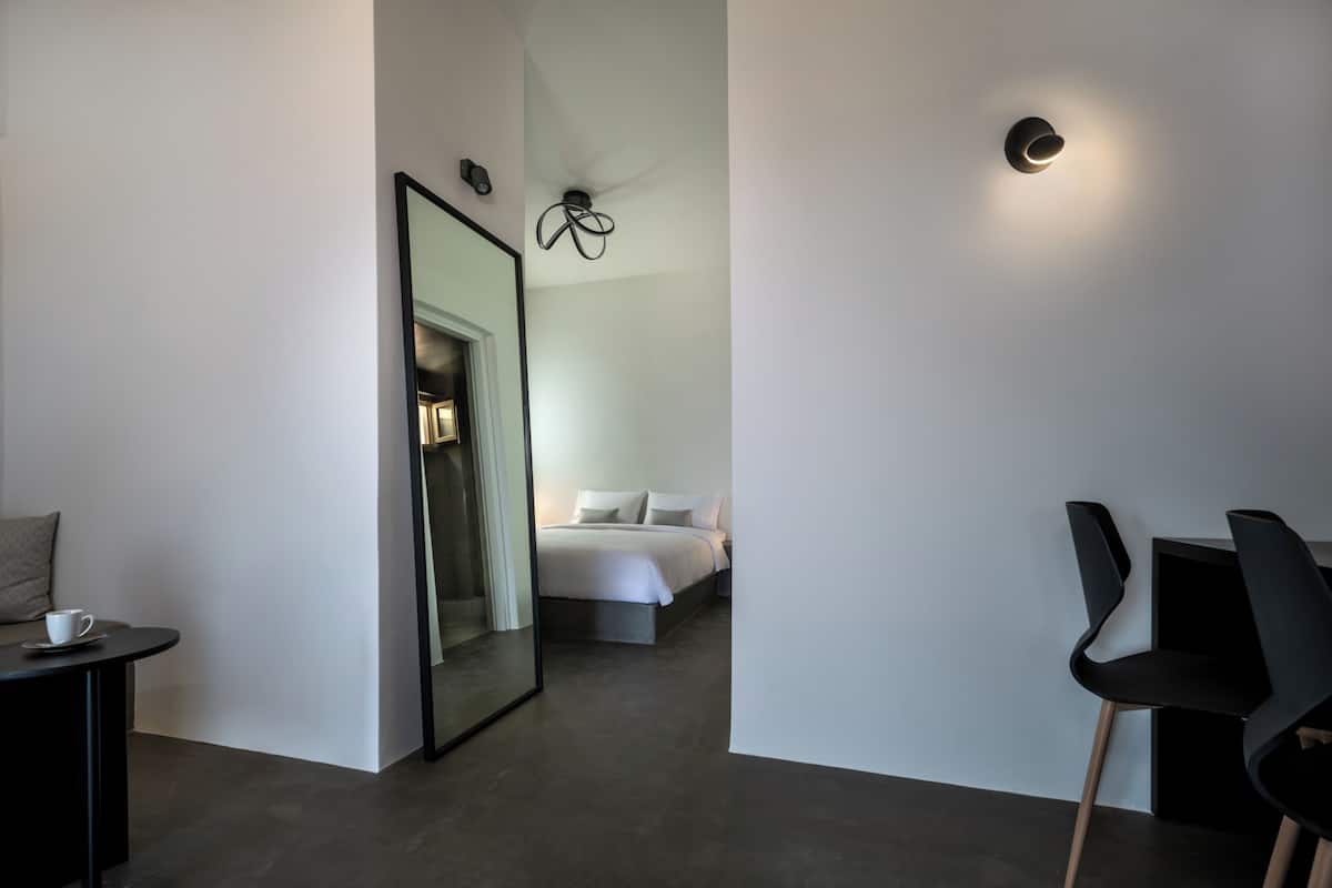 A modern hotel room with a large mirror, a bed, a small table with a cup, and black chairs.