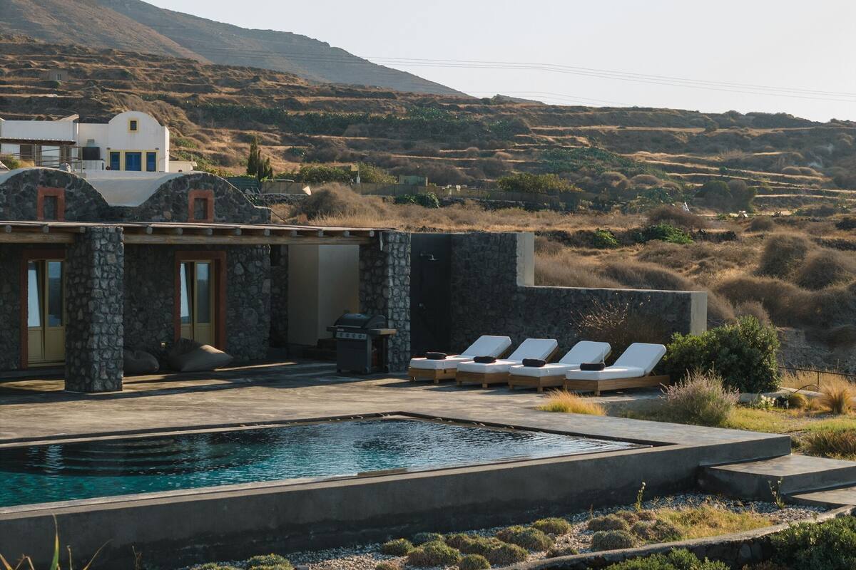 A pool area with lounge chairs, a barbecue, and a view of the surrounding landscape.