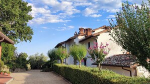 Casa rural con camino de grava, rodeada de vegetación y un cielo despejado.