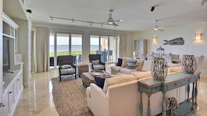 A spacious living room with a large window, a ceiling fan, and a view of the ocean.