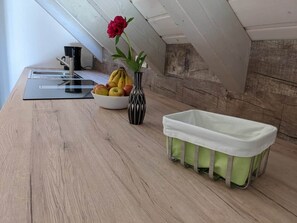 A kitchen with a wooden countertop, a black and white vase with flowers, a fruit bowl, and a white baby bathtub.