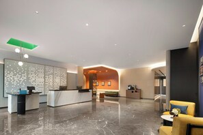 A modern hotel lobby with a reception desk, seating area, and a view of the interior.