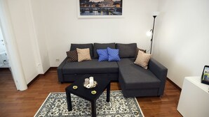 Ett modernt vardagsrum med en hörnsoffa, ett soffbord och en inramad målning som föreställer en stadsbild på väggen.
