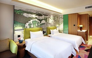 Ein Hotelzimmer mit zwei Betten, einem grünen Sessel, einem kleinen Tisch mit einer Vase und einem Wandgemälde.
