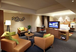 Ein Hotelzimmer mit einem Bett, zwei Sofas, einem Schreibtisch mit Computer, einem Fernseher und einer Lampe.