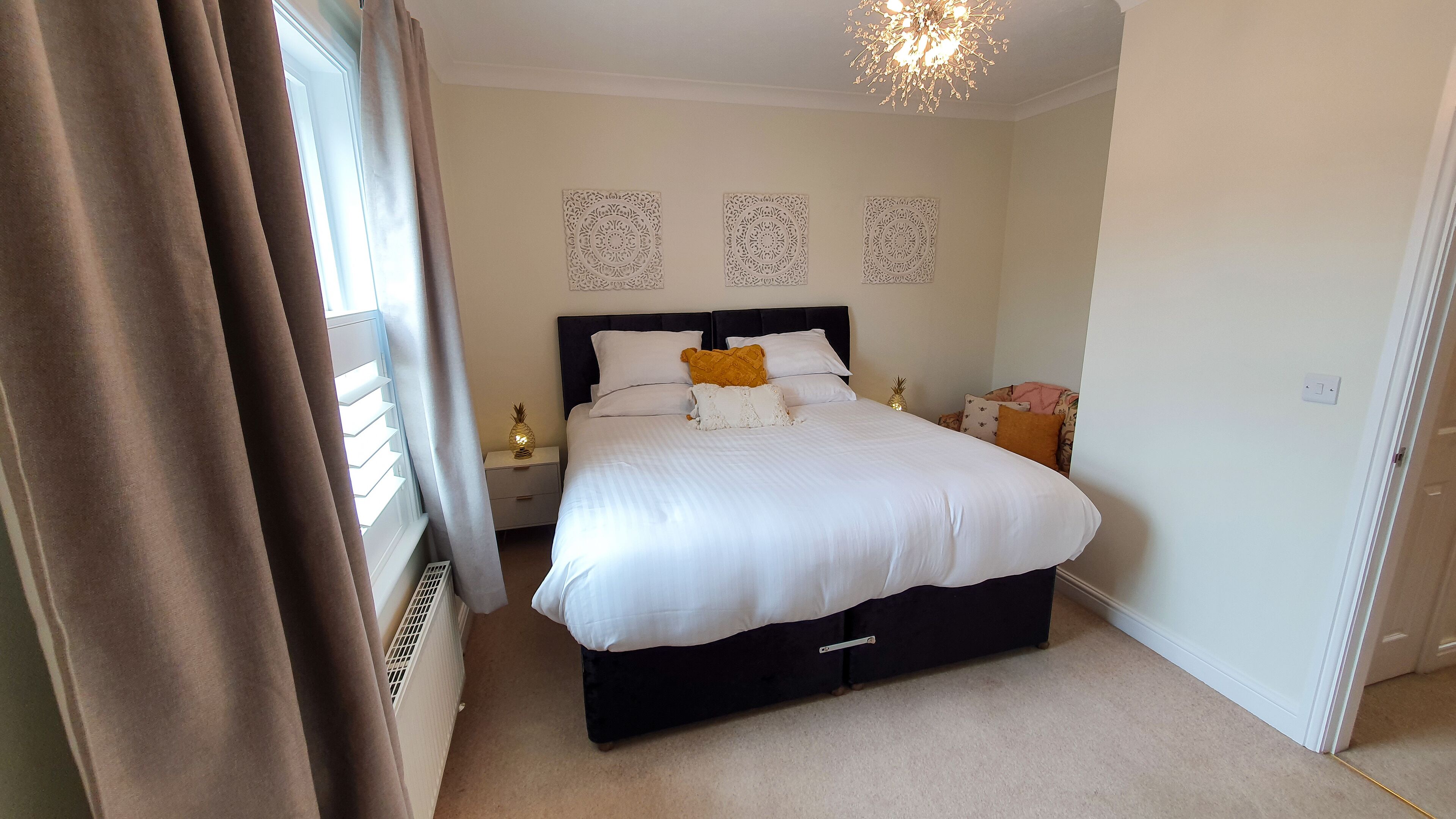 Un dormitorio con cama, mesitas de noche, lámpara de noche, una piña decorativa y un aplique de techo.