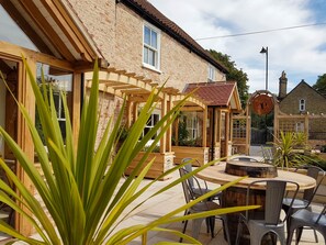 A patio area with a wooden pergola, a round wooden table, and metal chairs.