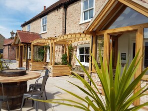A patio area with a wooden table and chairs, surrounded by brick walls and wooden pergolas. - The Adam & Eve (Market Rasen)