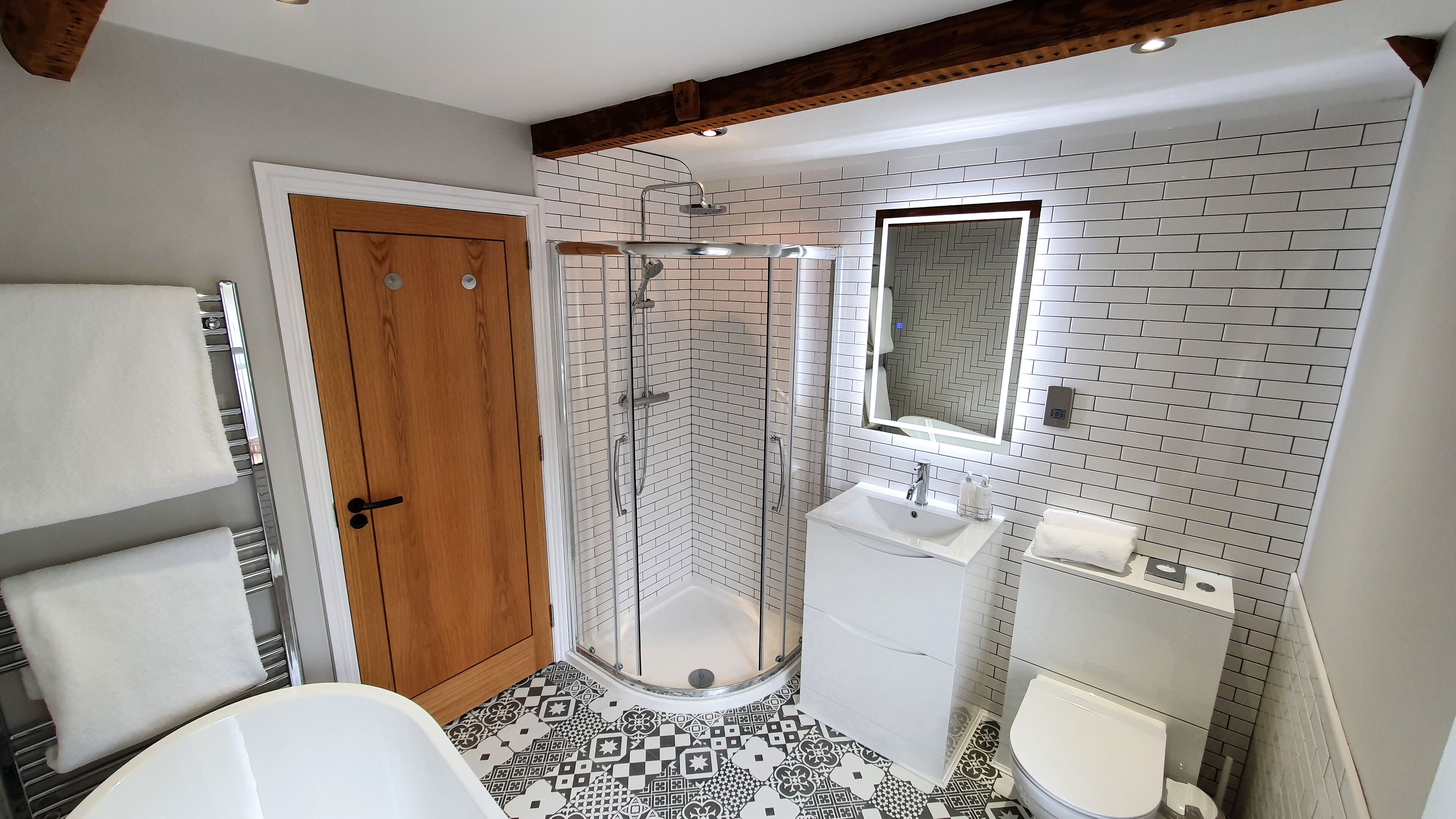 Un baño con puerta de madera, ducha envuelta en vidrio, lavamanos blanco y un inodoro.