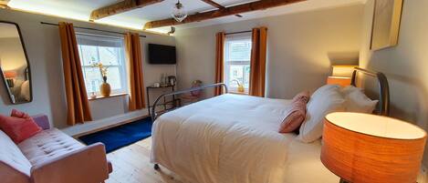 A hotel room with a bed, a chair, a bedside table, a lamp, and a TV.