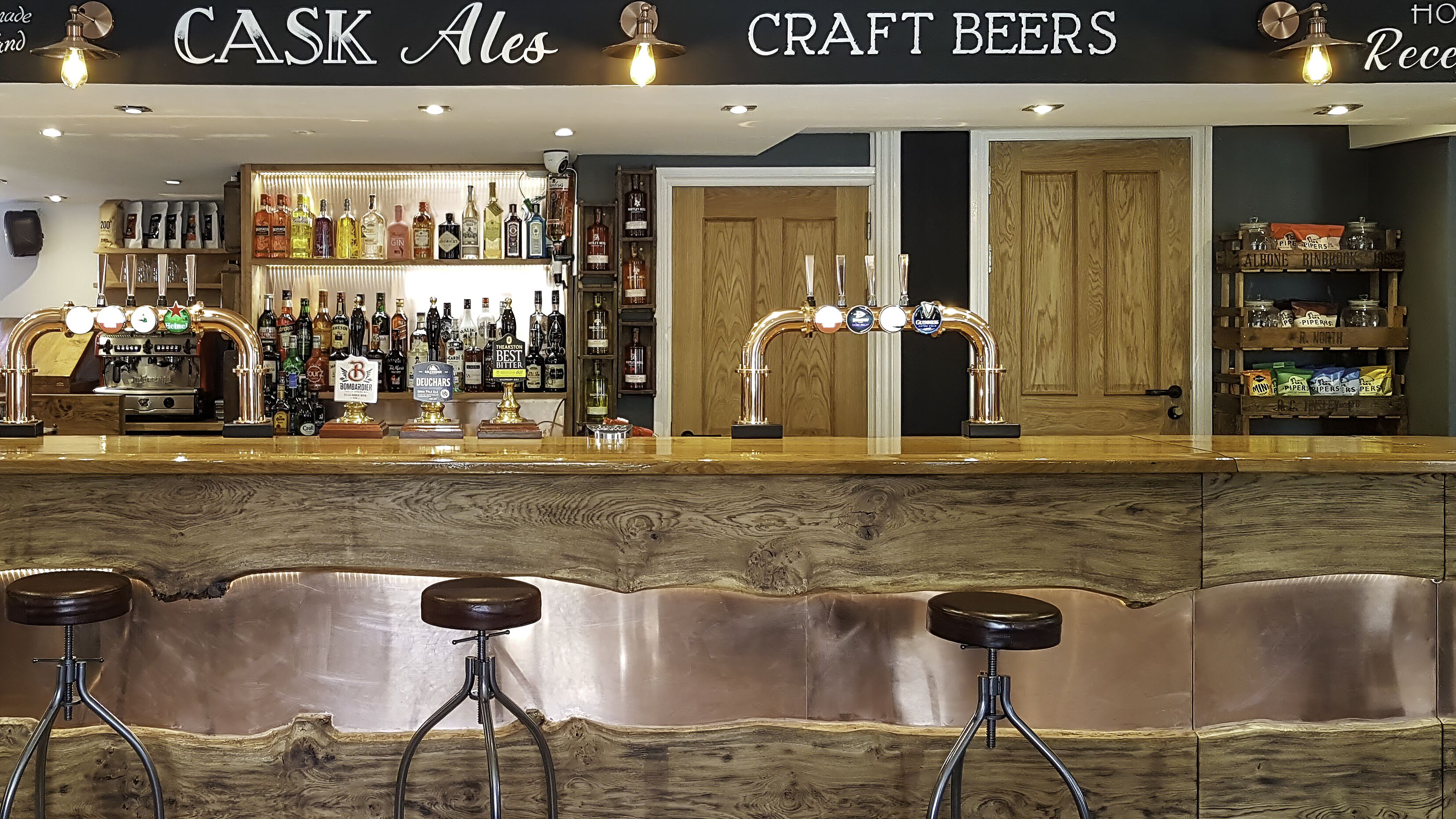 Zona de bar con mostrador de madera, taburetes y una variedad de cervezas artesanales.