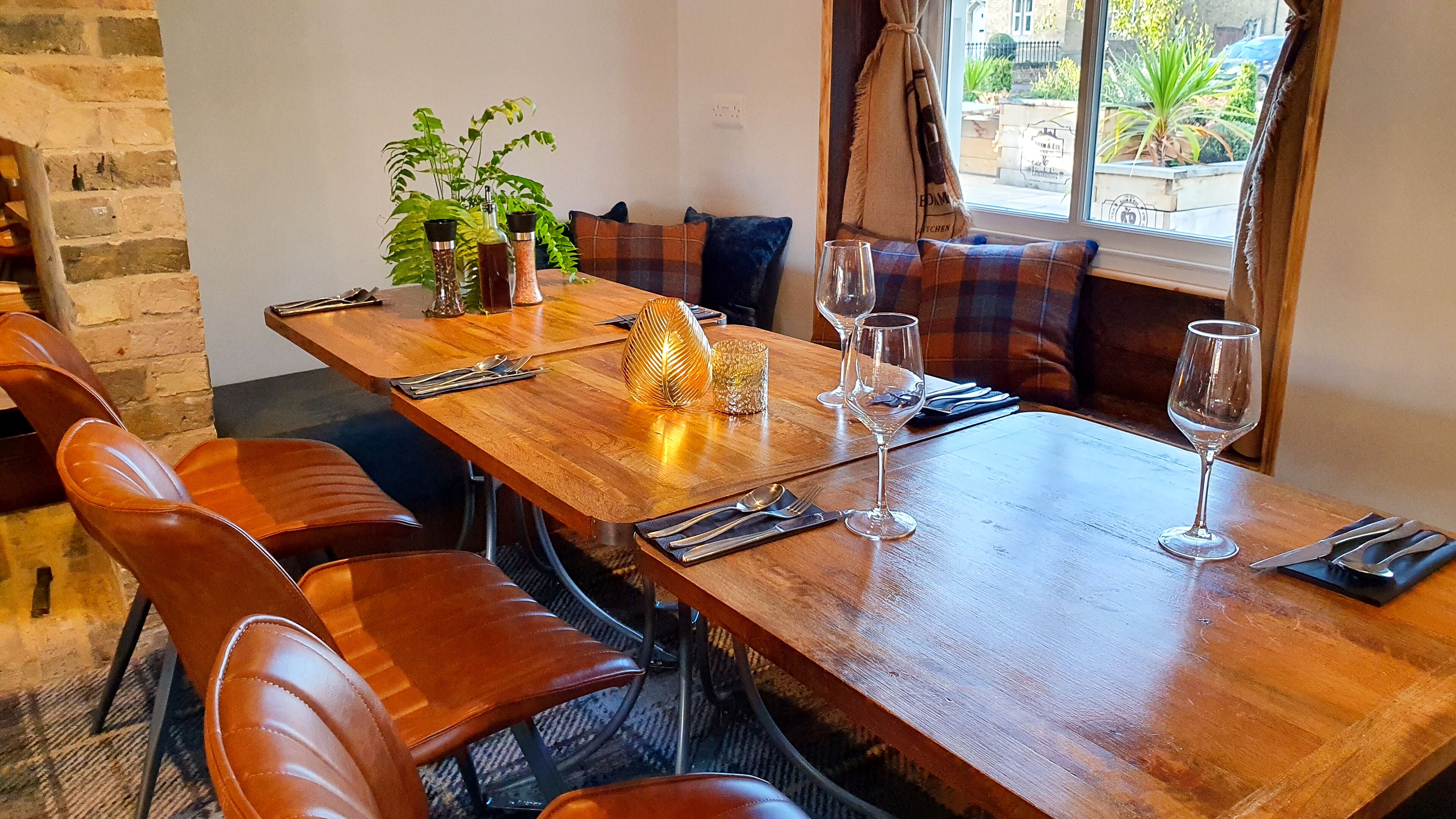 Mesa de jantar de madeira posta com cadeiras, planta e copos de vinho.