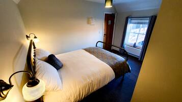 A hotel room with a bed, a bedside lamp, a window with curtains, and a door.