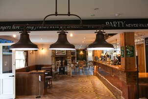 Uma área de bar com piso de madeira, banquetas e luminárias pendentes.
