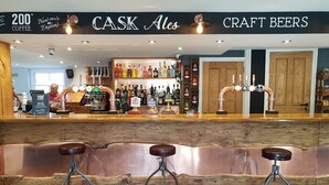 A bar area with a wooden counter, stools, and a variety of bottles and glasses.