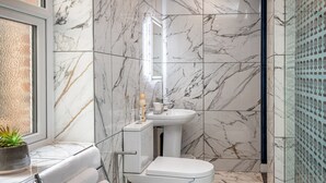 Une salle de bain moderne avec des carreaux de marbre, une douche en verre, un lavabo blanc et un porte-serviettes.